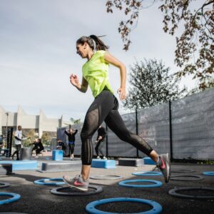 woman in green tank top and black leggings doing yoga on blue round trampoline